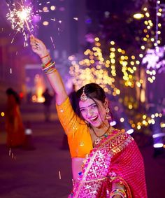 a woman in an orange and pink sari holding sparklers