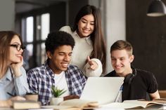 three young people sitting at a table looking at a laptop computer and pointing to the screen