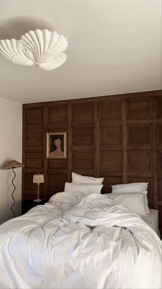 a large bed with white sheets and pillows in a bedroom next to a painting on the wall