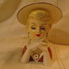 a ceramic figurine wearing a hat and holding her hands to her face on a white tablecloth