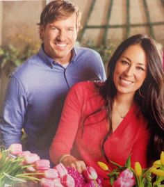 a man and woman standing next to each other with flowers in front of them on a table