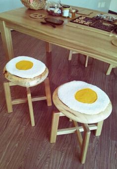 two fried eggs sitting on top of wooden stools next to a table with utensils