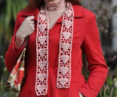 a woman wearing a red coat and scarf with her hands in her pockets while holding a purse