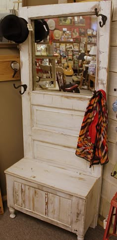 an old white bench with a coat rack and hat hanging on the wall next to it