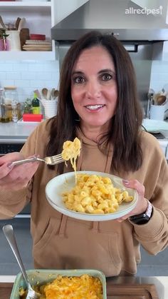 a woman holding a plate of macaroni and cheese with a fork in her hand