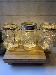 three mason jars with fairy lights in them sitting on a wooden stand next to a potted plant