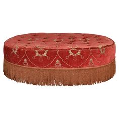 a round red ottoman with fringe trim around the top and bottom, on a white background