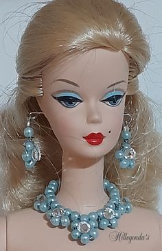 a doll with blonde hair and blue eyes is wearing a necklace made out of pearls