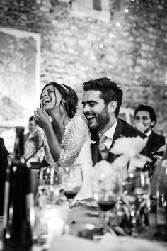 the bride and groom laugh as they sit at their wedding reception table in black and white