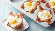 some eggs and bacon are in the muffin tins on a blue wooden table