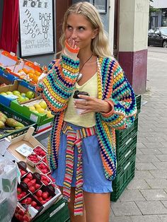 a woman standing in front of a fruit stand holding a cell phone to her mouth