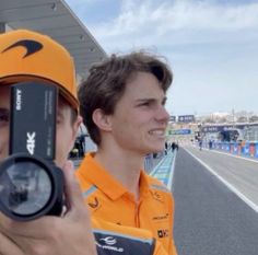 two men in orange shirts and hats taking pictures with their cell phones on the track