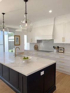 a large kitchen with an island in the middle and two lights hanging from the ceiling