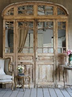 an old wooden room with two chairs and a table in front of the doors that lead to another room