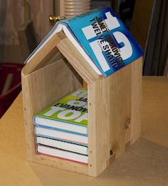 a wooden house shaped like a book holder with books in it on top of a table