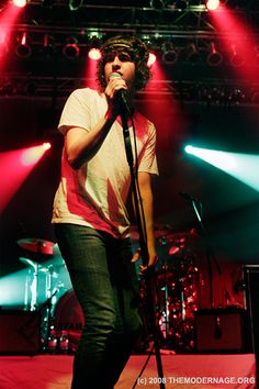 a man standing on top of a stage holding a microphone in front of red and green lights