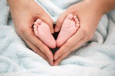 a person holding their baby's feet in the shape of a heart on a blanket