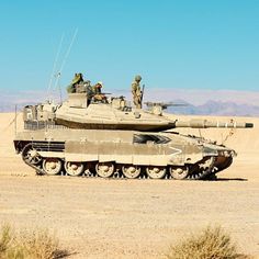 an army tank driving through the desert with two soldiers on it's back end