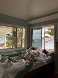 two people laying in bed looking out the window at the ocean and palm trees outside