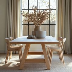 a table with two chairs and a vase on it in front of a window filled with curtains