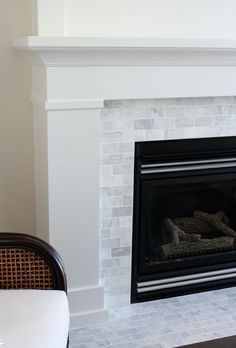 a white fireplace with a black mantle and chair