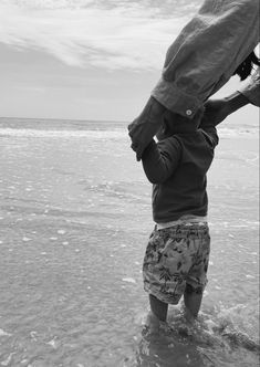 a young child standing in the ocean holding onto an adult's hat over his head