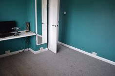 an empty room with a computer on the desk and shelves in front of it that are painted teal green