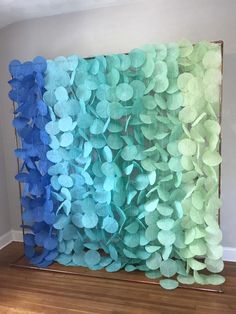 some blue and green paper flowers are hanging on a wooden frame in front of a wall