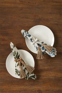 two white plates topped with tassels on top of a wooden table