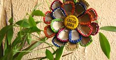 a flower made out of bottle caps sitting on top of a green plant next to a wall