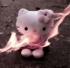 a hello kitty stuffed animal sitting on top of a fire filled ground with its eyes open