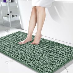 a person standing on a bath mat in front of a white toilet and tub with green rugs