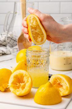 someone is squeezing orange juice into a jar with lemons on the counter next to it