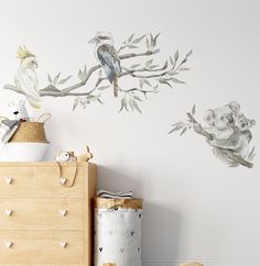 two birds sitting on top of a tree branch next to a white wall with koala bears