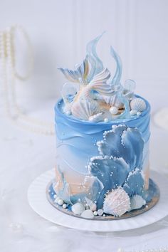 there is a blue and white cake with shells on the top, along with pearls around the edges