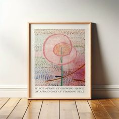 a framed art print with a pink flower in the center on a wooden floor next to a white wall