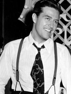 a man in suspenders and a tie smiling for the camera with his hands on his hips