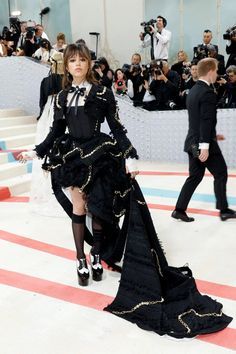 a woman in a black dress standing on the runway with cameras around her and people taking pictures