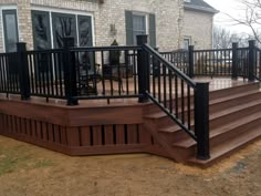 a wooden deck with black railings and hand rails next to a brick house in the background