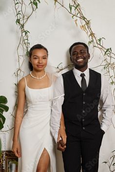 a man and woman standing next to each other in front of a wall with vines