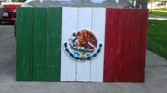 a wooden sign with the flag of mexico painted on it's side in front of a house