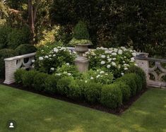 a garden with white flowers and greenery in the center, surrounded by bushes and stone benches