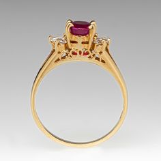 a gold ring with an oval shaped ruby stone surrounded by smaller round diamonds