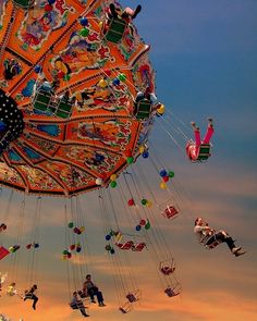 several people are flying in the air on a colorful carnival swing ride at sunset or dawn