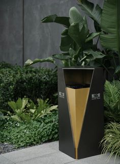 a black and gold vase sitting on top of a cement floor next to green plants