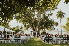 an outdoor ceremony with white folding chairs and palm trees in the foreground, overlooking water