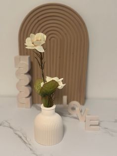 a white vase with flowers in it sitting on a table next to the word love