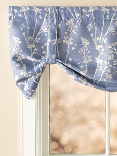 a window with a blue flowered valance hanging from it's side next to a window sill