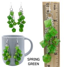 a mug with some green cubes hanging from it's side next to a pair of earrings