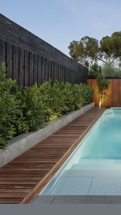 an empty swimming pool surrounded by greenery next to a wooden deck and fenced in area